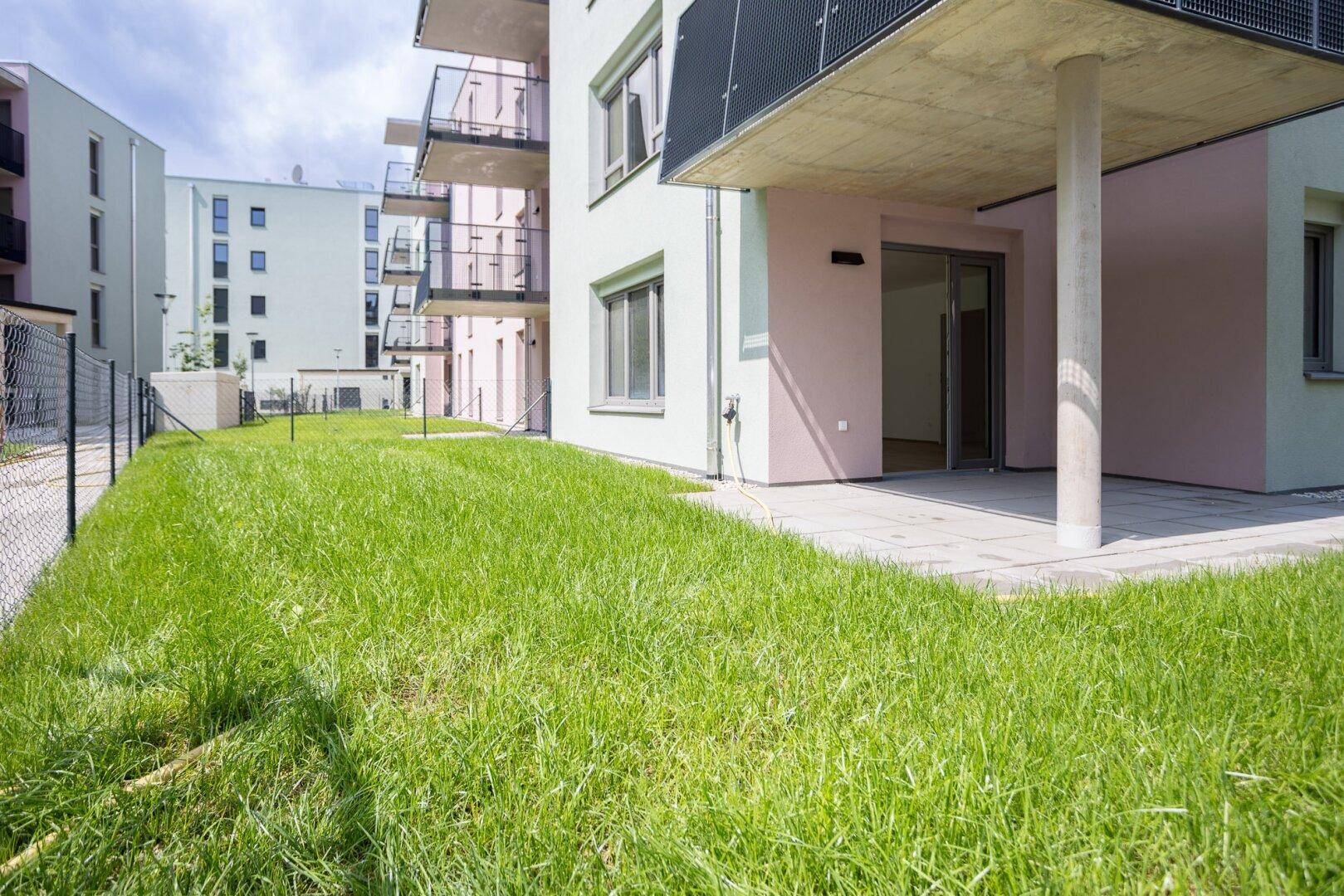 Erdgeschoss-Terrasse mit direktem Zugang zu einer kleinen Rasenfläche in einer modernen Wohnanlage.