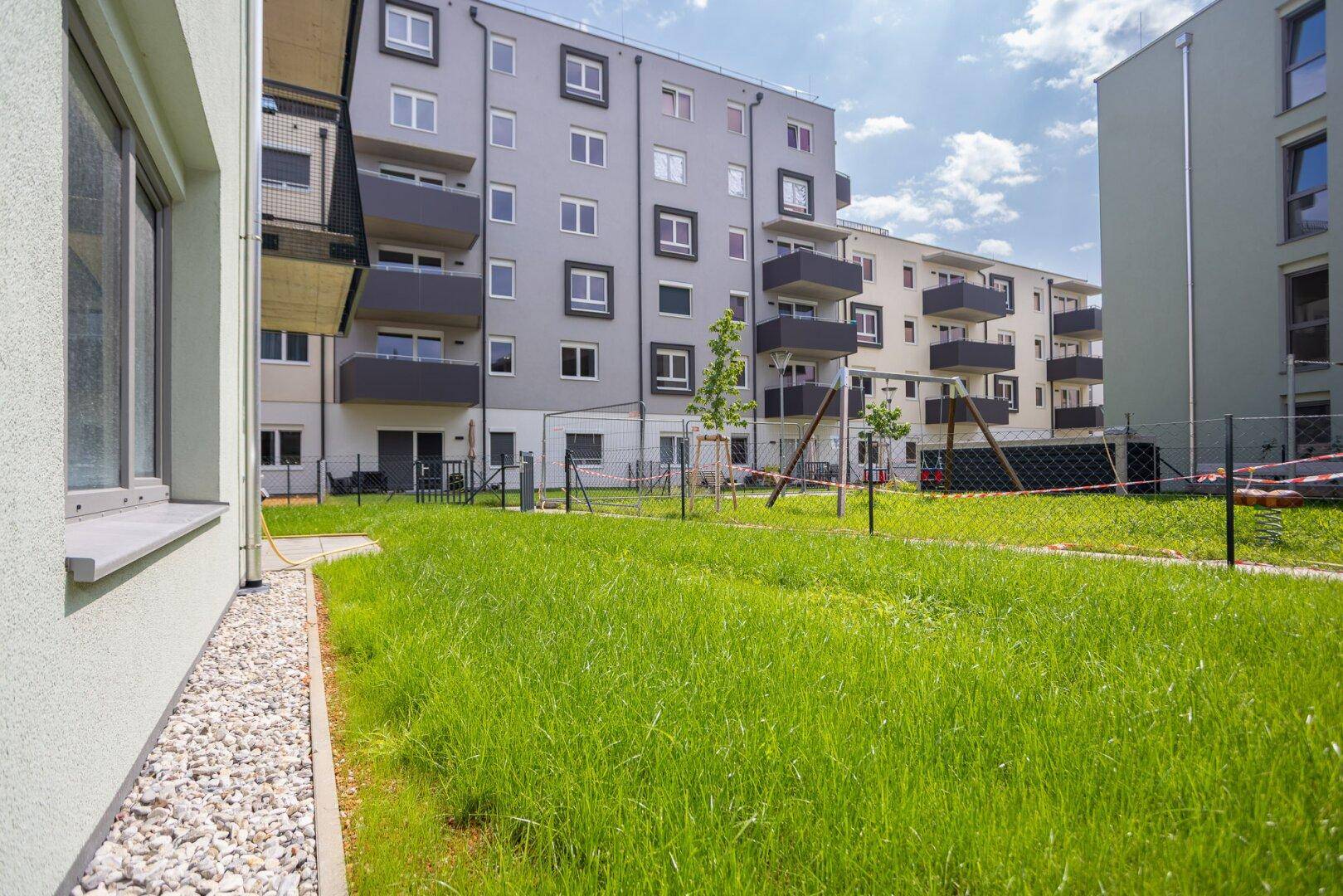 Gemeinschaftliche Grünfläche mit Spielplatz und modernen Wohngebäuden im Hintergrund.