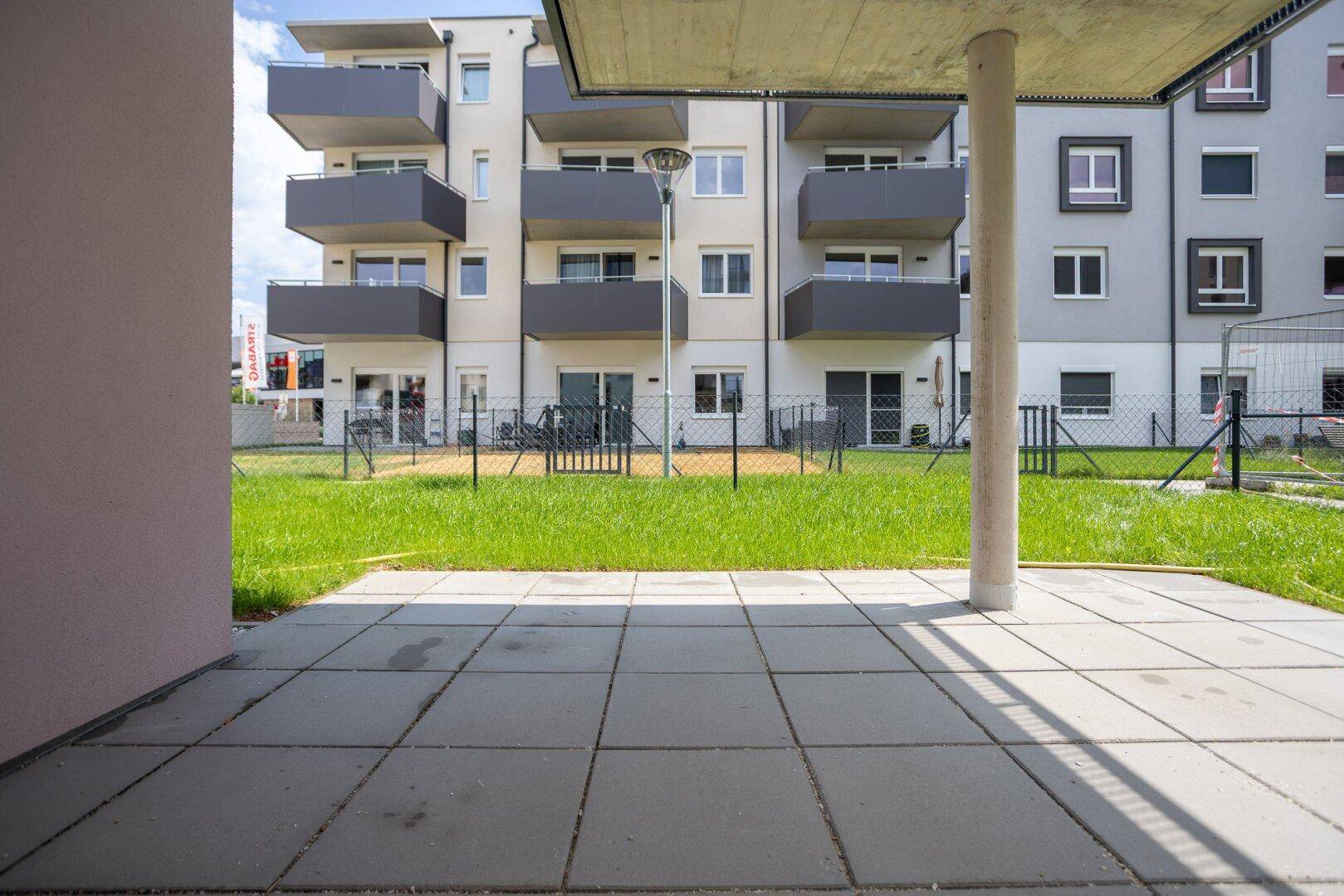 Geräumige Terrasse mit Blick auf die gepflegte Rasenfläche und die umliegenden Neubauten.