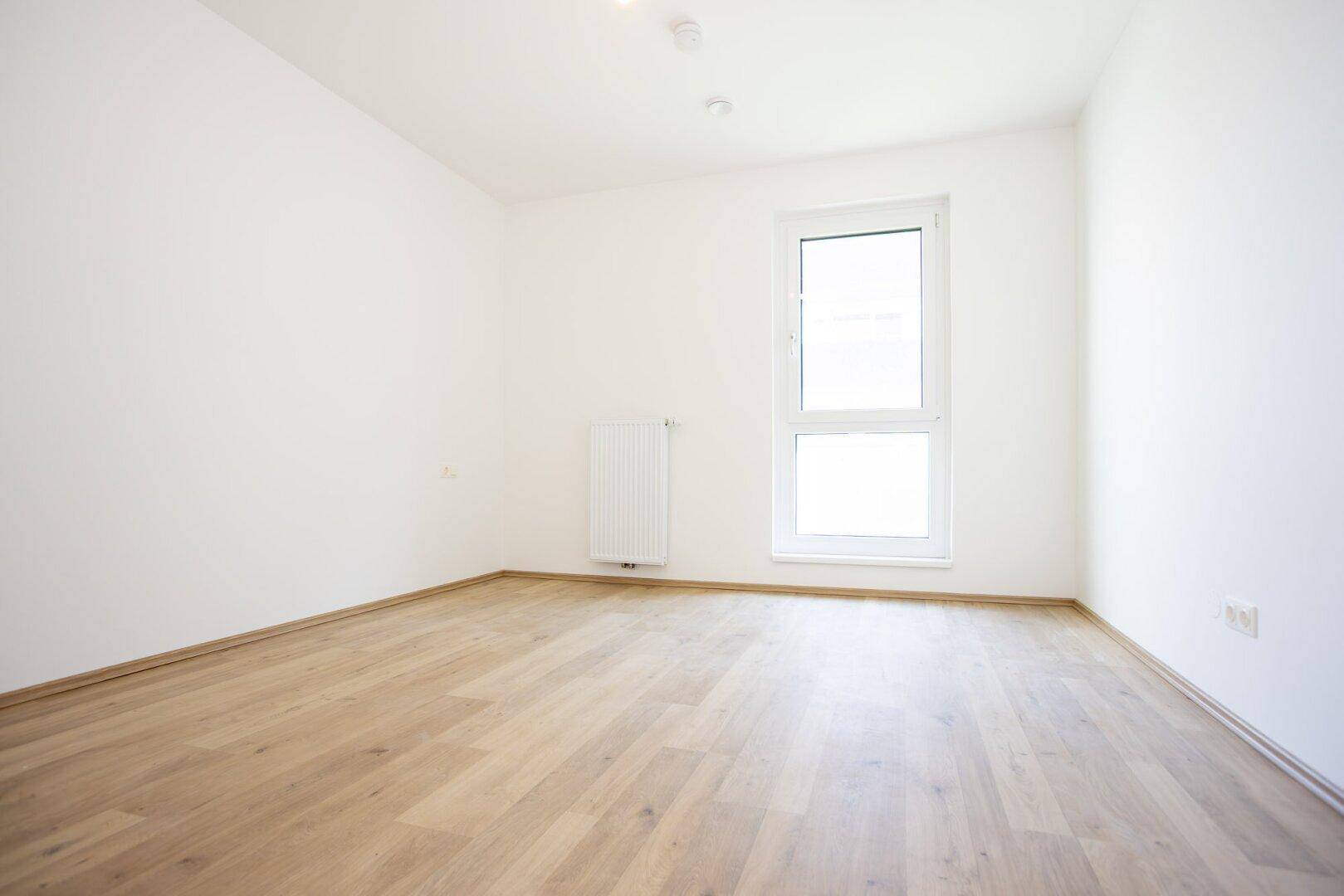 Ruhiges Schlafzimmer mit hellem Laminatboden, weiß gestrichenen Wänden und einem großen Fenster.