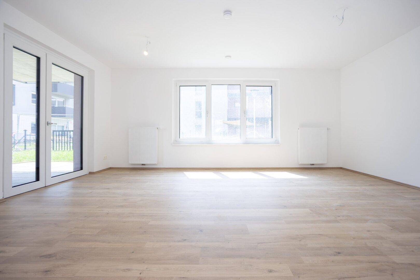 Heller Wohnbereich mit großen Fenstern und Zugang zur Terrasse, ausgestattet mit modernem Laminatboden.