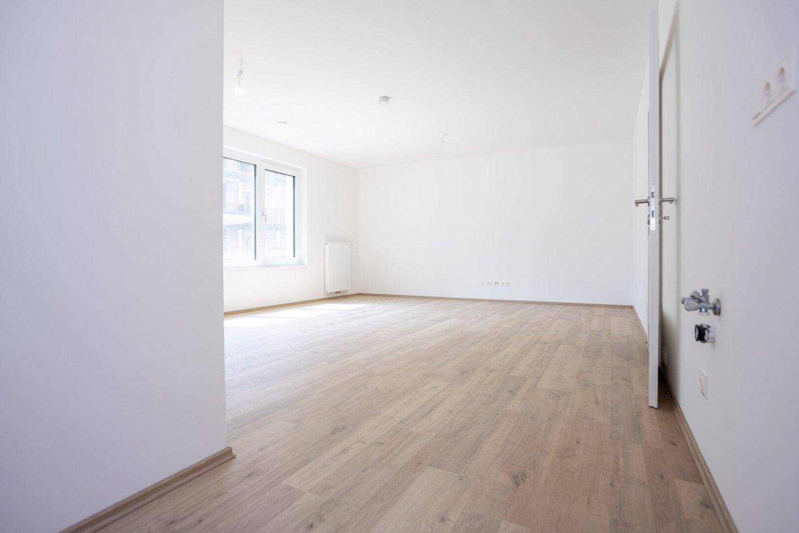 Heller Flur mit Laminatboden und weißen Wänden, der zu weiteren Räumen führt.