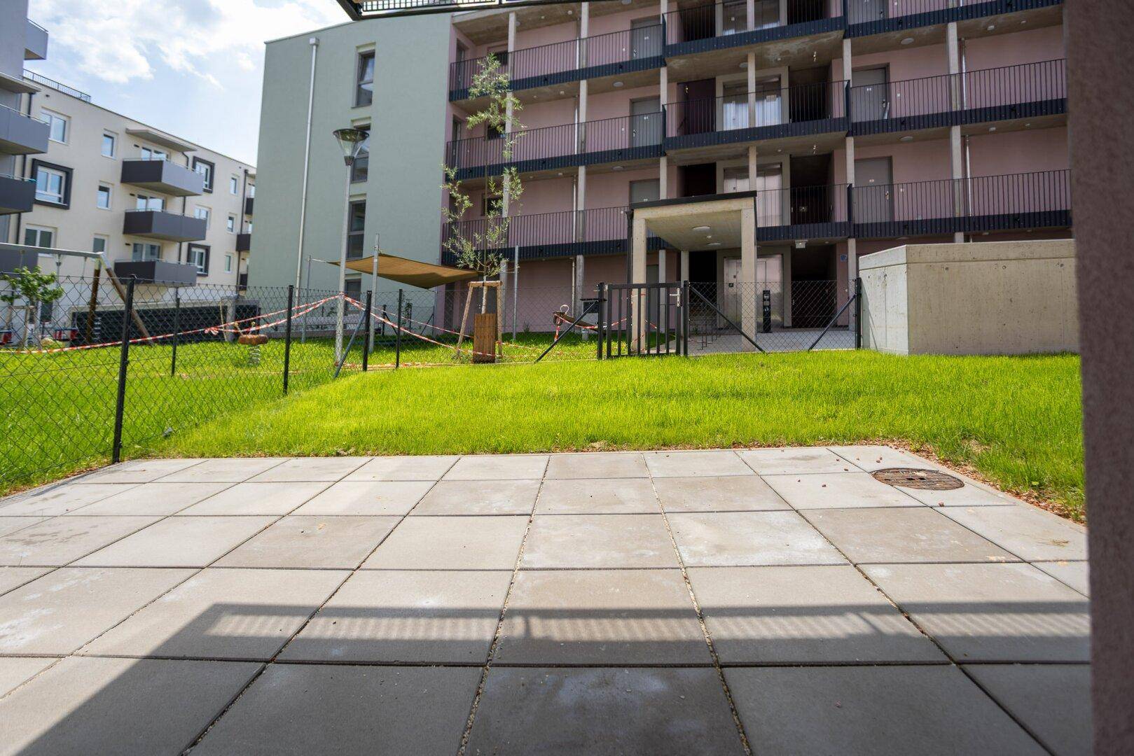 Gepflasterte Terrasse mit Blick auf den Gemeinschaftsgarten und die umliegenden Wohngebäude.