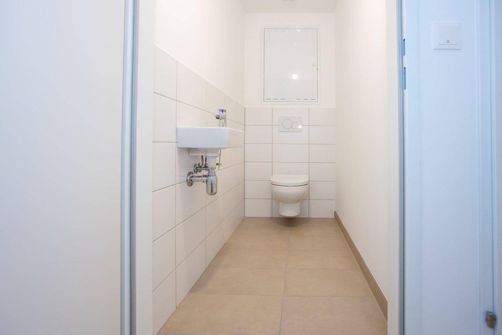 Funktionelles Gäste-WC mit wandhängender Toilette, kleinem Waschbecken und weißen Fliesen.