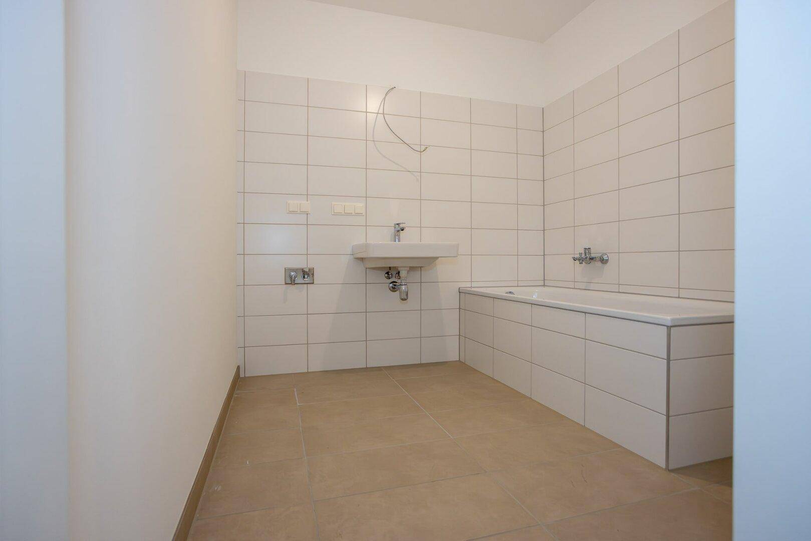 Modernes Badezimmer mit weißen Wandfliesen, Waschbecken und einer Badewanne.