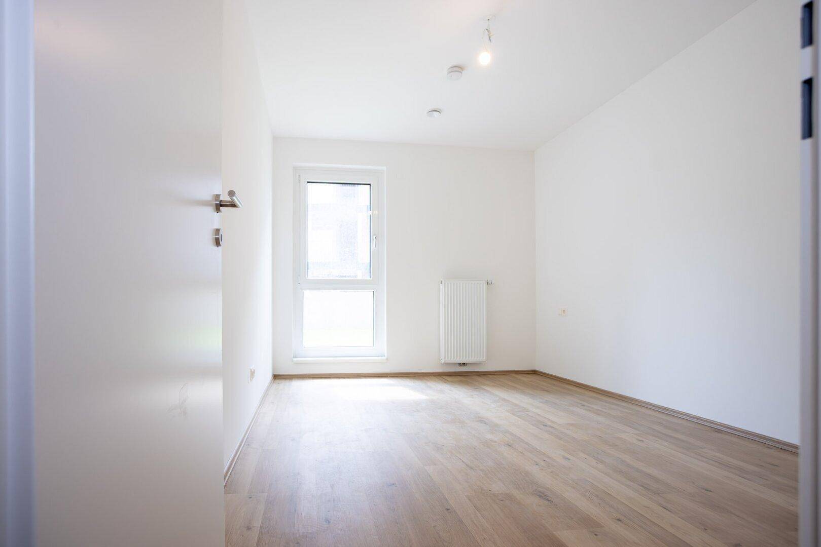 Ruhiges, helles Zimmer mit Laminatboden und einem großen Fenster, ideal als Schlaf- oder Arbeitszimmer.