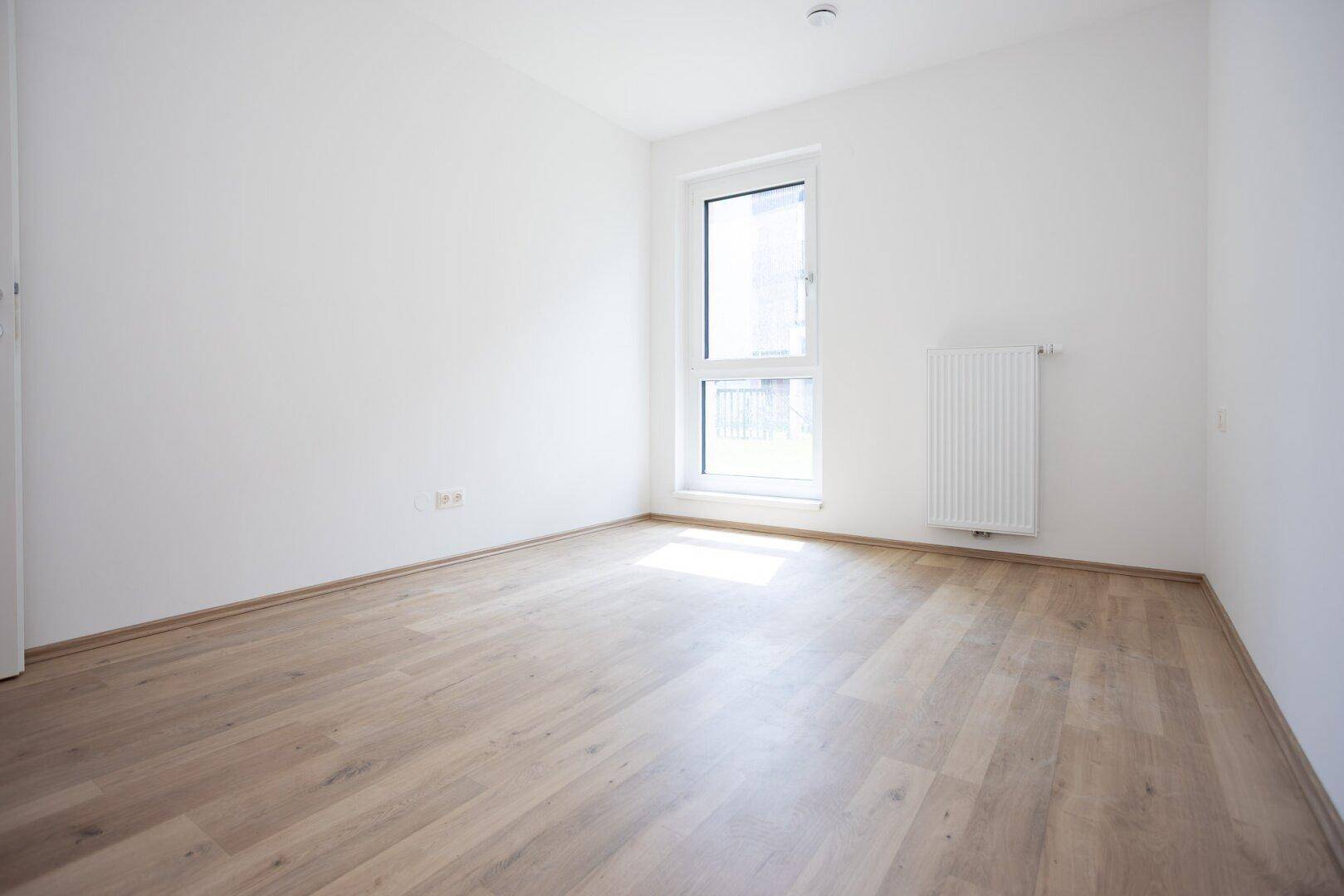 Freundliches, leeres Zimmer mit hellem Laminatboden und einem Fenster, bereit zur individuellen Gestaltung.