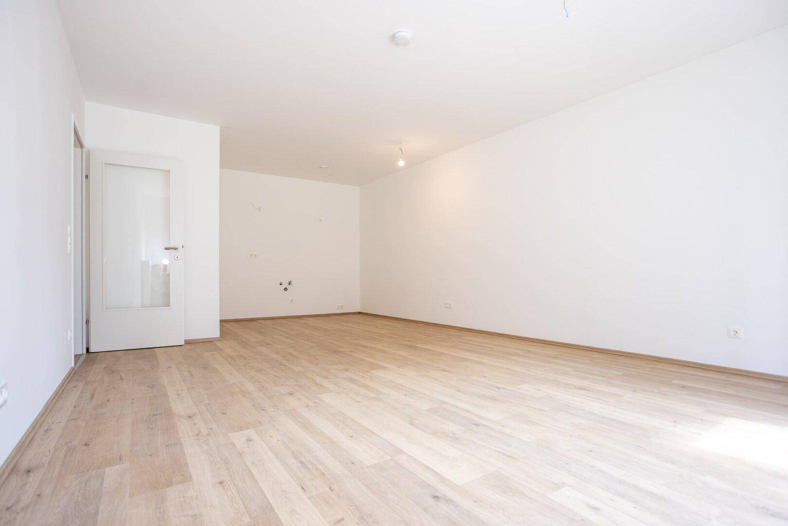 Geräumiger, unmöblierter Küchenbereich mit Laminatboden und vorbereiteten Anschlüssen.