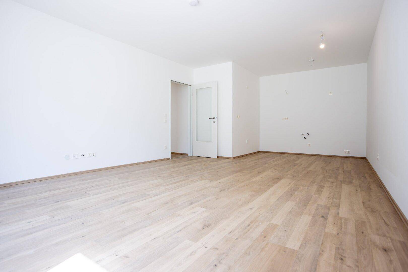 Leerer Küchenbereich mit Laminatboden und Anschlüssen für eine zukünftige Einbauküche.