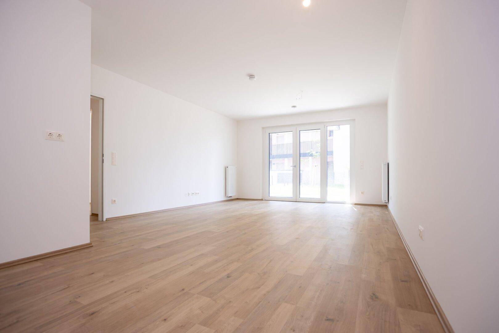 Geräumiger, heller Wohnbereich mit Zugang zur Terrasse und modernem Holzboden.