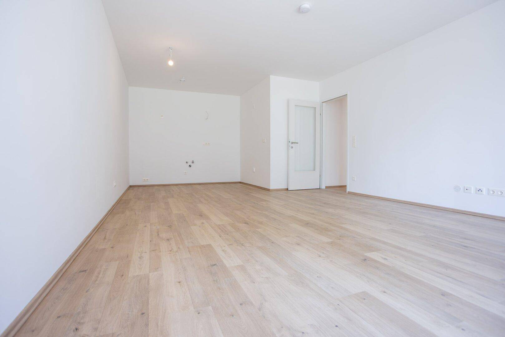 Heller, unmöblierter Raum mit Holzboden und weiß gestrichenen Wänden.