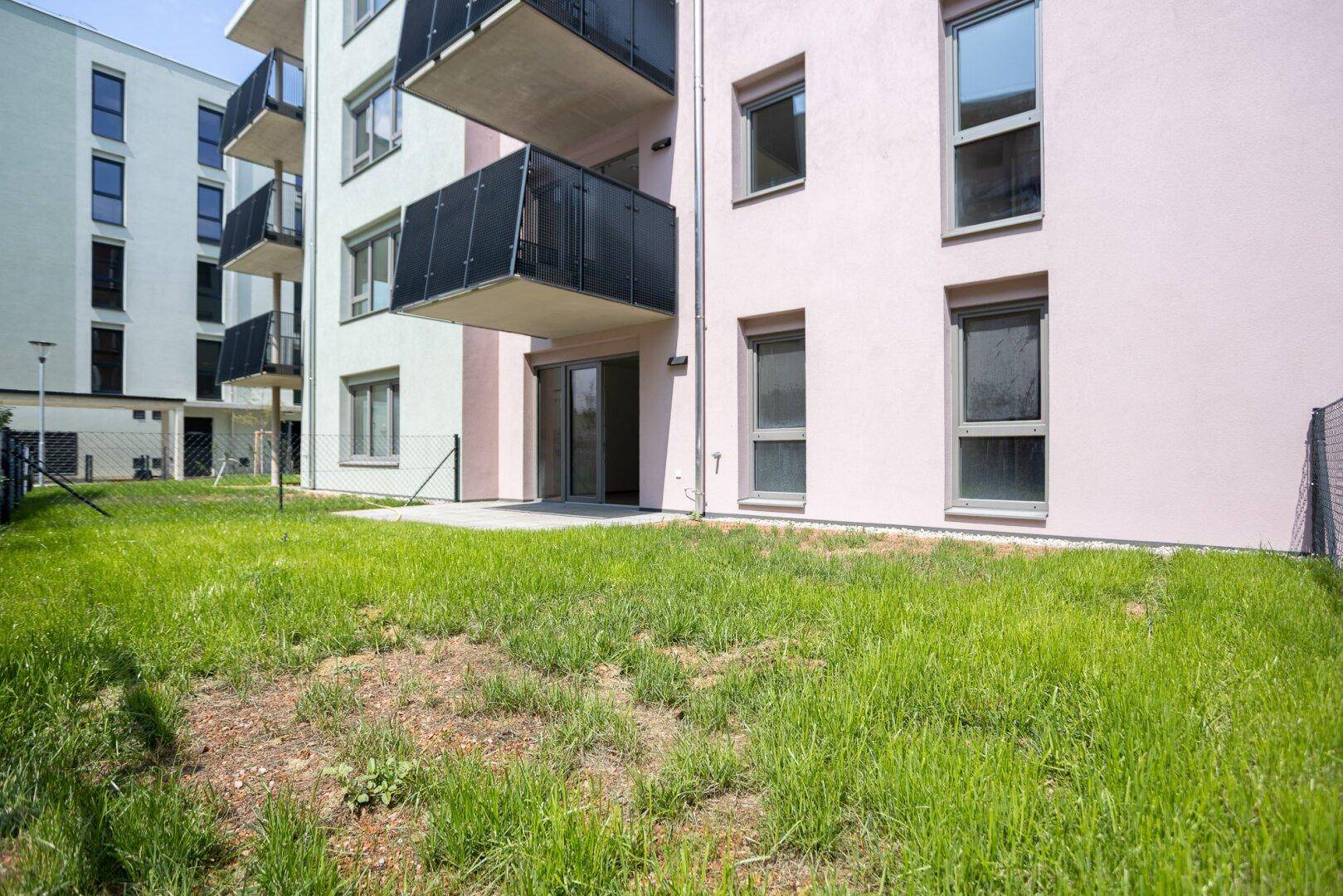 Erdgeschosswohnung mit privater Terrasse und Rasenfläche, umgeben von einer modernen Wohnanlage.