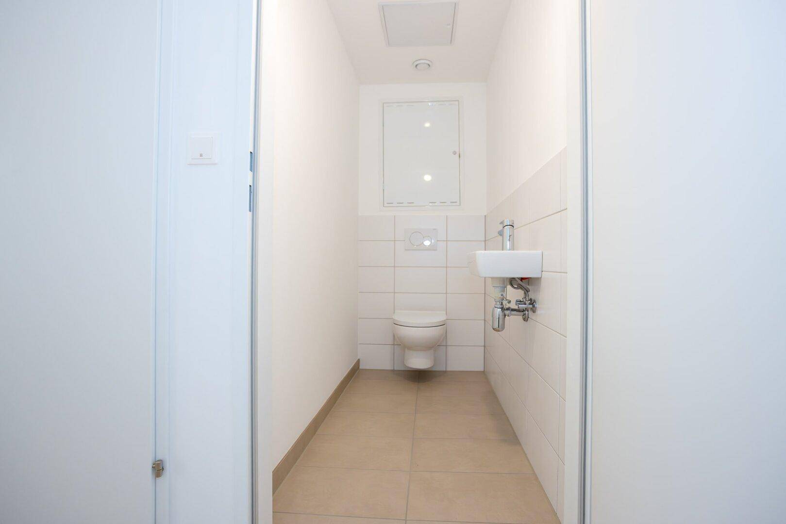 Kleines Gäste-WC mit wandhängender Toilette, kleinem Waschbecken und weißen Fliesen.