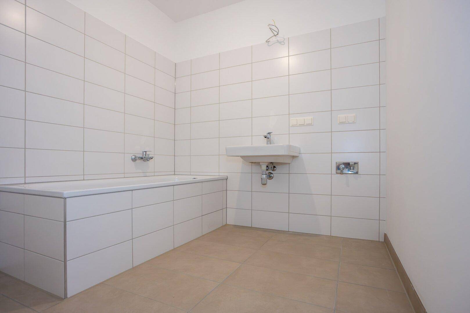 Helles Badezimmer mit Badewanne, Waschbecken und weißen Wandfliesen, bereit zur Fertigstellung.