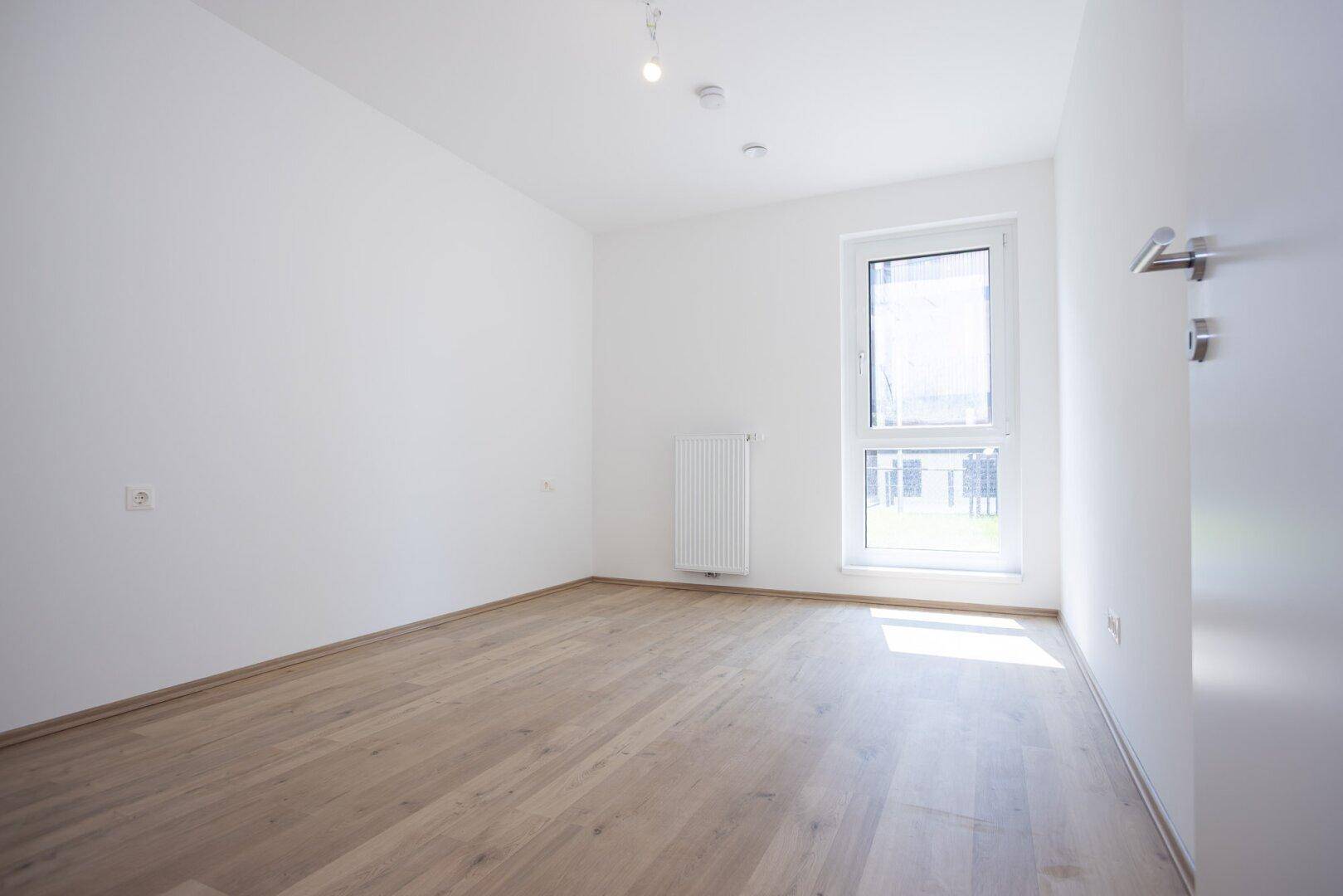 Leeres Zimmer mit großem Fenster und hellem Holzboden, ideal als Schlaf- oder Arbeitszimmer.