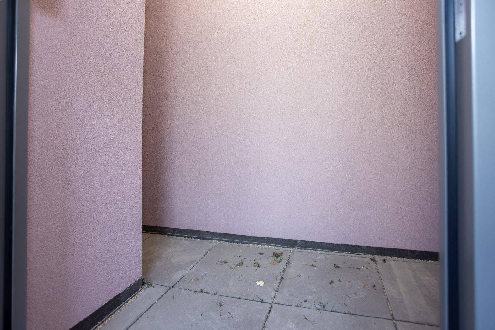 Kleiner, gefliester Innenraum mit rosa Wänden und dunklem Sockel.