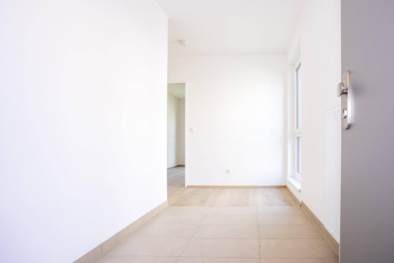 Heller Eingangsbereich mit Fliesenboden und weiß gestrichenen Wänden in einem Neubau.