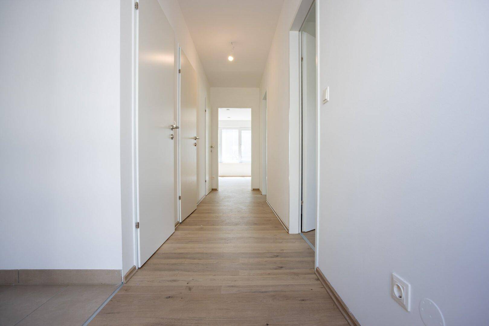 Langer, heller Flur mit Laminatboden und mehreren Türen zu den angrenzenden Räumen.