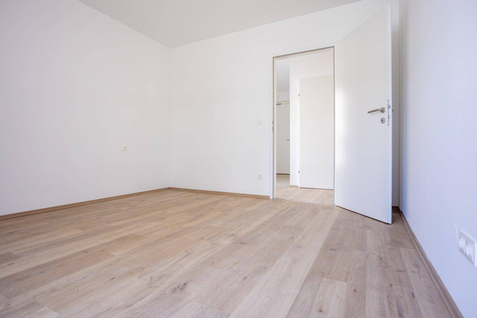 Leeres Schlafzimmer mit hellem Laminatboden und weiß gestrichenen Wänden.