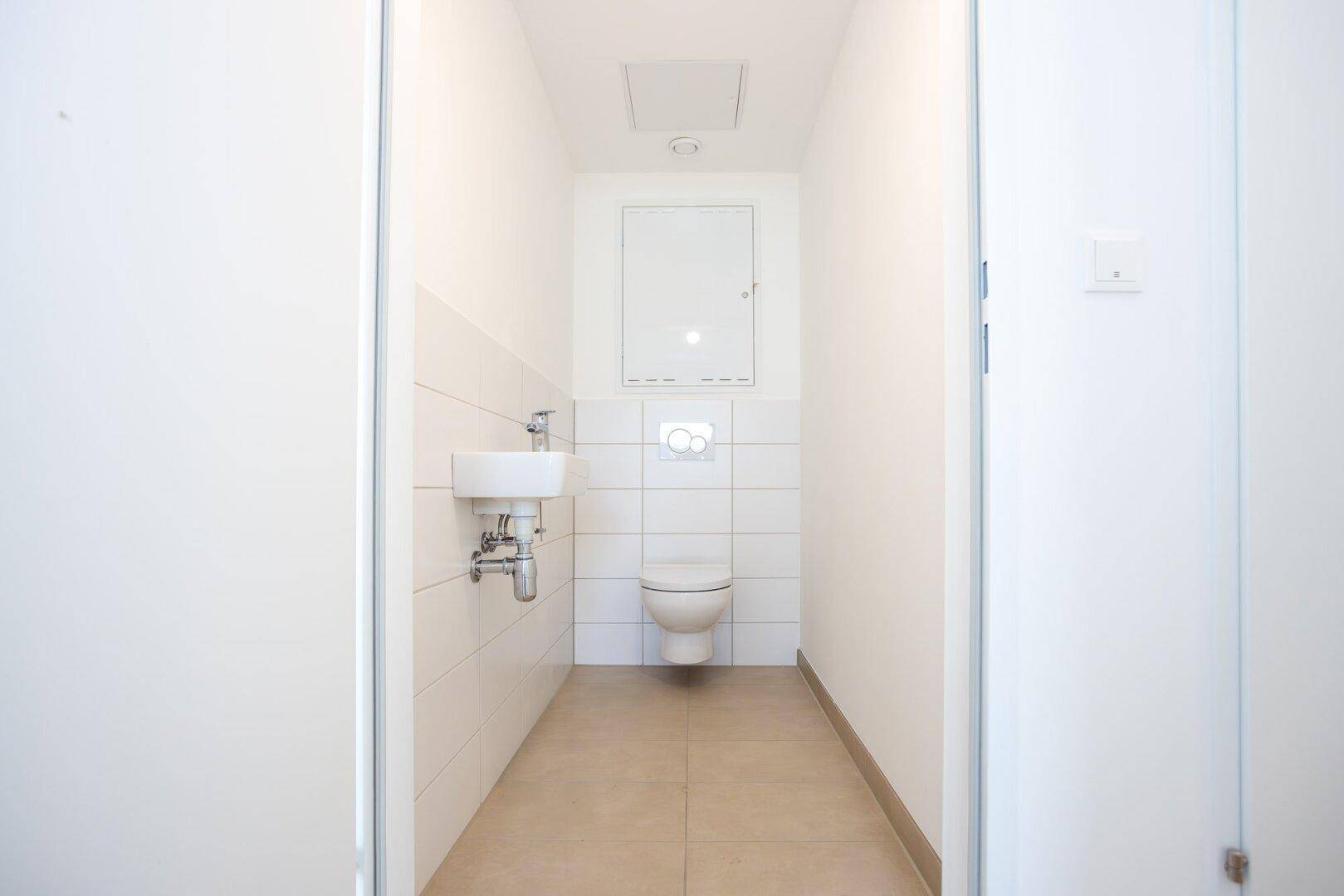 Kleines Gäste-WC mit Wand-WC, Waschbecken und hellen Fliesen.