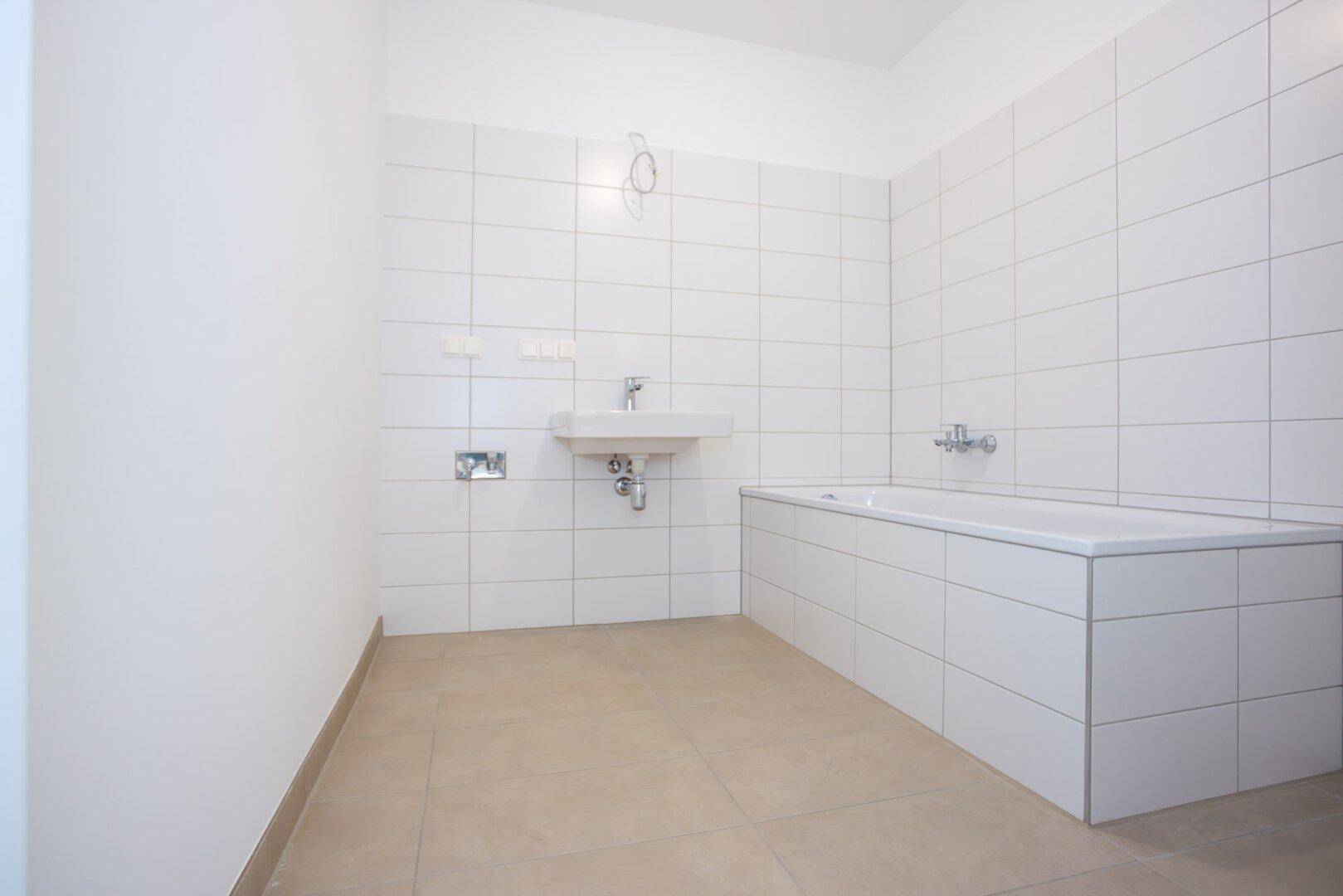 Helles Badezimmer mit weißen Wandfliesen, Badewanne und Waschbeckenanschluss.