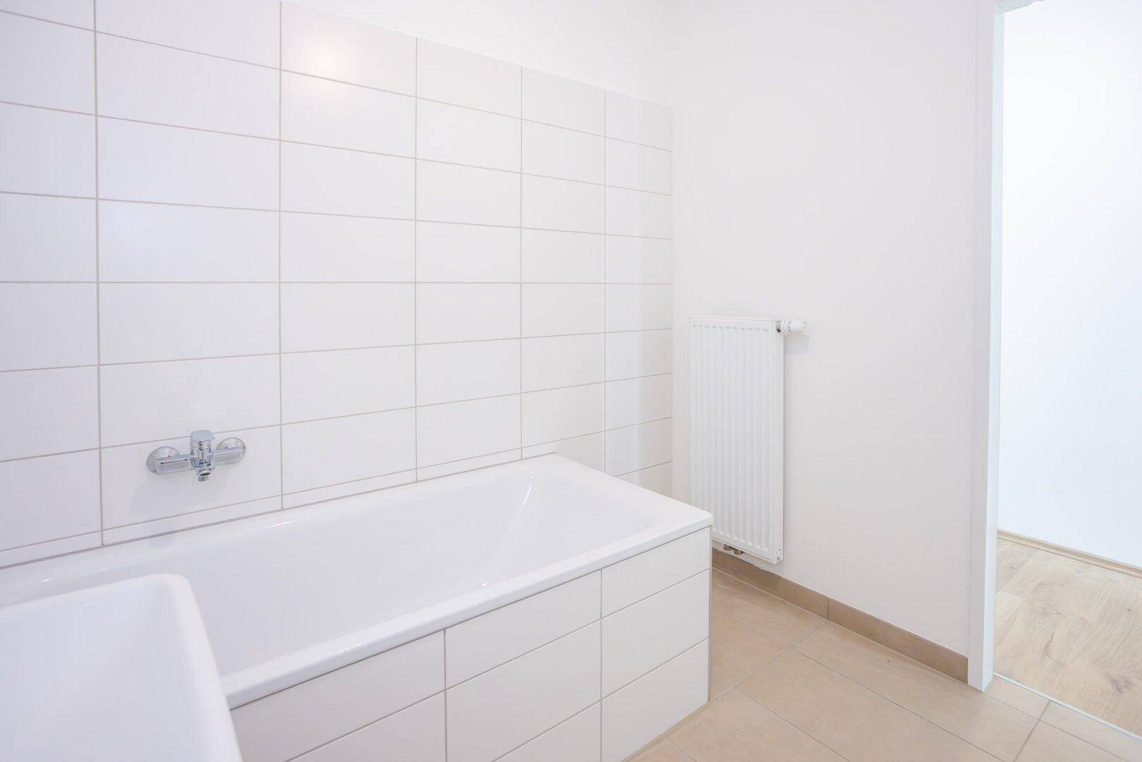 Modernes Badezimmer mit weiß gefliesten Wänden, Badewanne und Heizkörper.