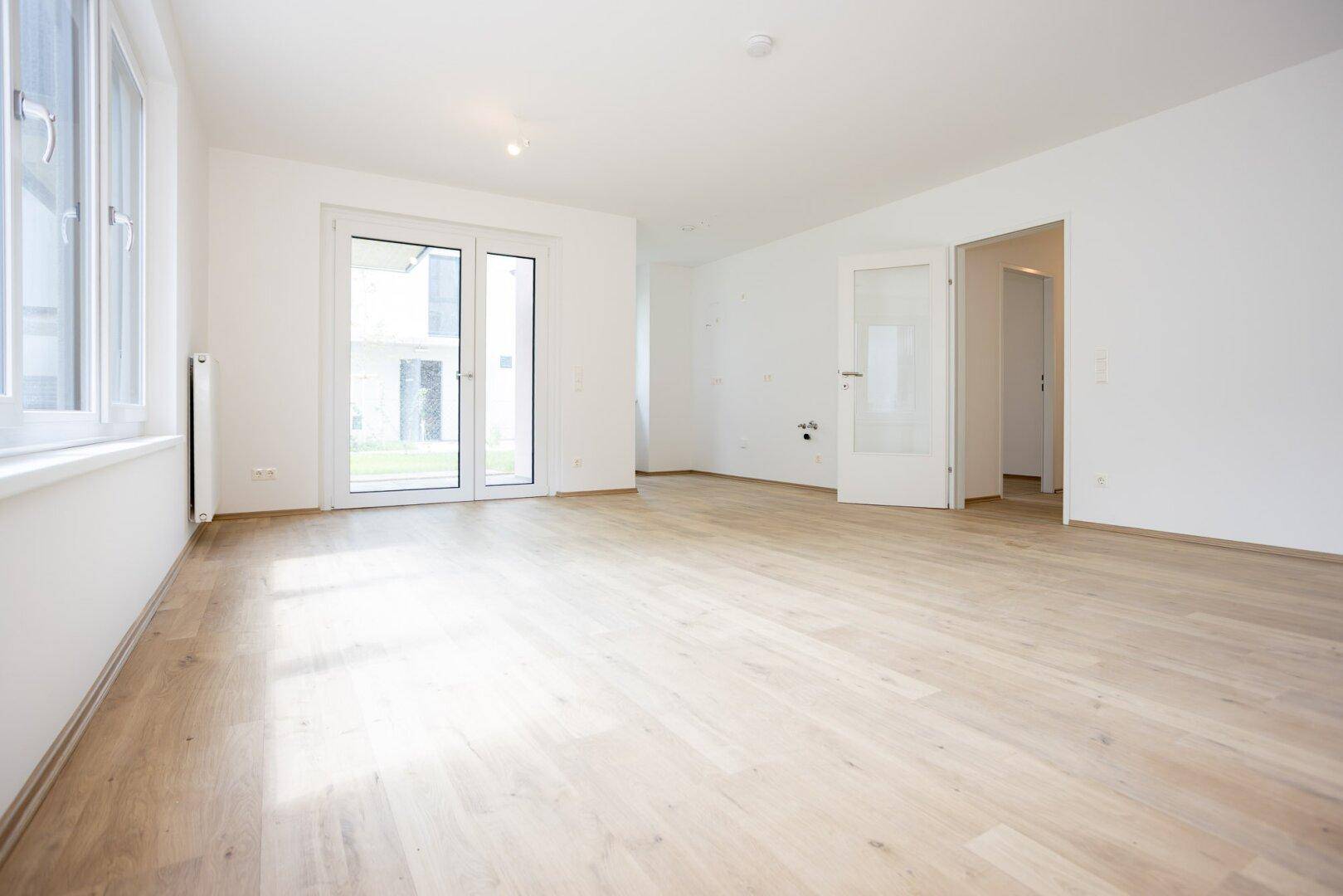 Geräumiger, heller Wohnbereich mit Laminatboden und Zugang zu einem Außenbereich.