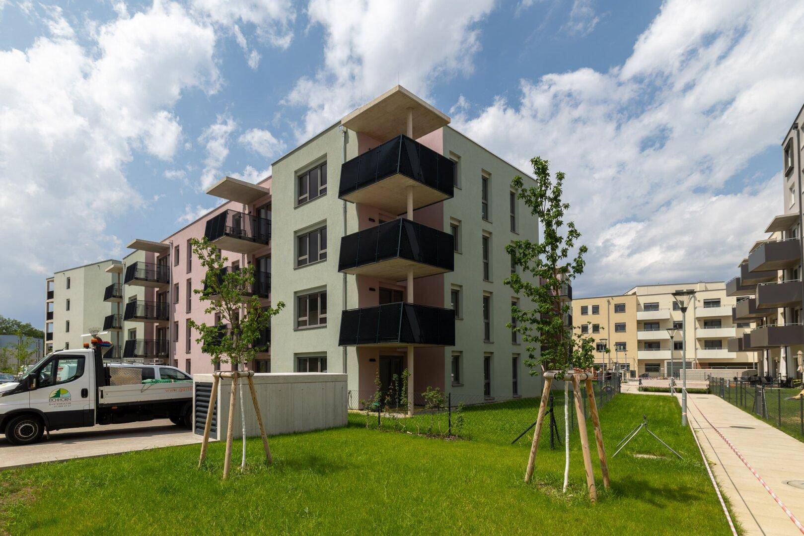 Moderne Wohngebäude mit Balkonen und einer Grünfläche, ein Lieferwagen parkt daneben.