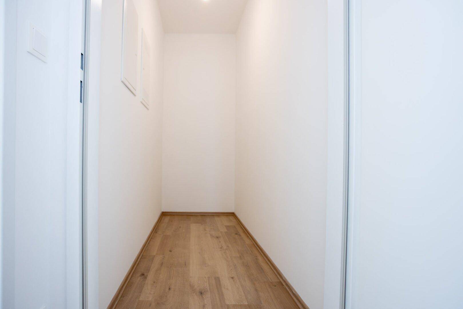 Schmaler, leerer Abstellraum mit Laminatboden und weißen Wänden, ideal für Lagerzwecke.