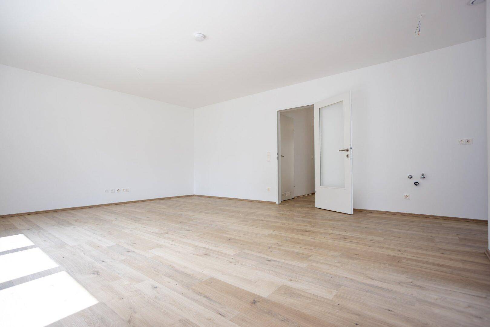 Leerer Küchenbereich mit Laminatboden und Anschlüssen für Spüle und Geräte.