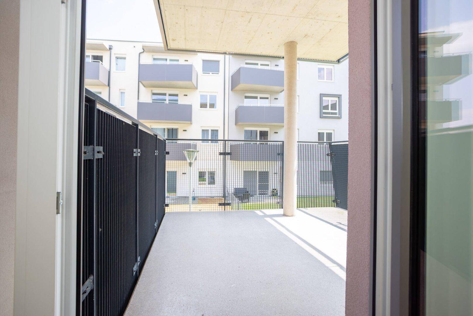 Blick vom Innenraum auf einen Balkon mit Metallgeländer und die umliegenden Wohngebäude.