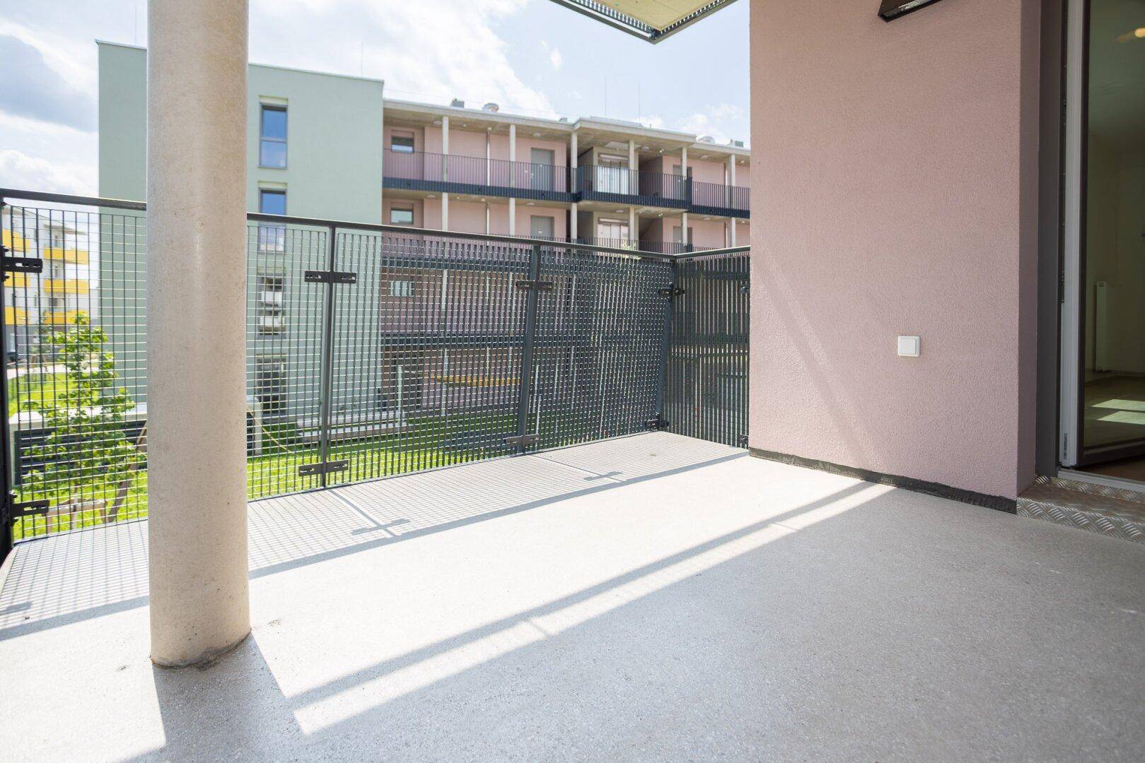 Geräumiger Balkon mit Betonboden und Metallgeländer, umgeben von modernen Wohngebäuden.