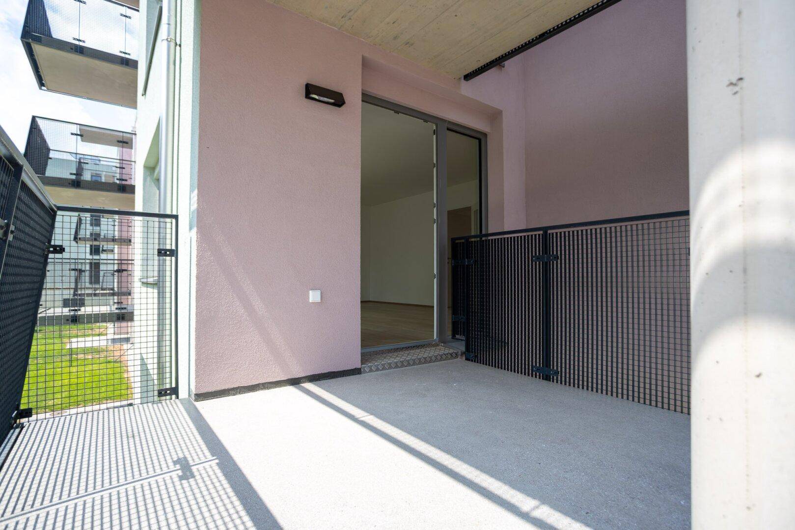 Balkon mit rosa Fassade, Betonboden und Metallgeländer, mit Blick auf die Nachbargebäude.