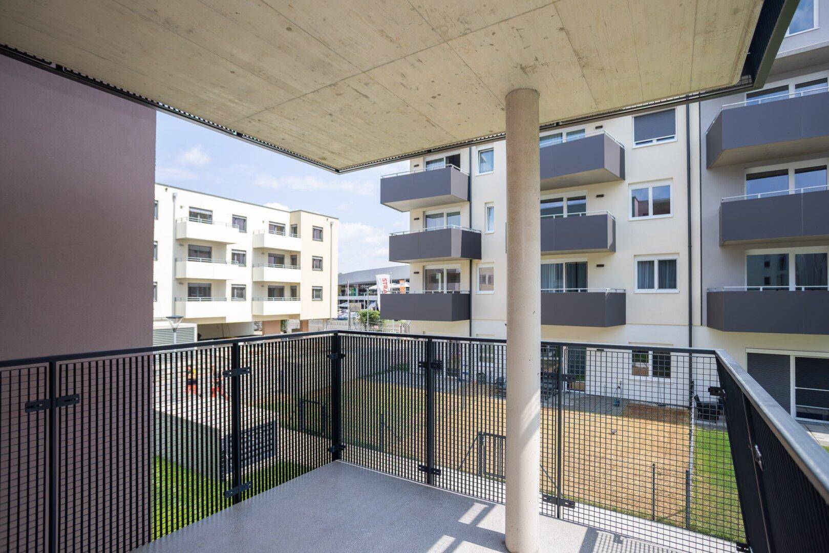 Balkon mit Betonboden und Metallgeländer, bietet einen weiten Blick auf die Wohnanlage.
