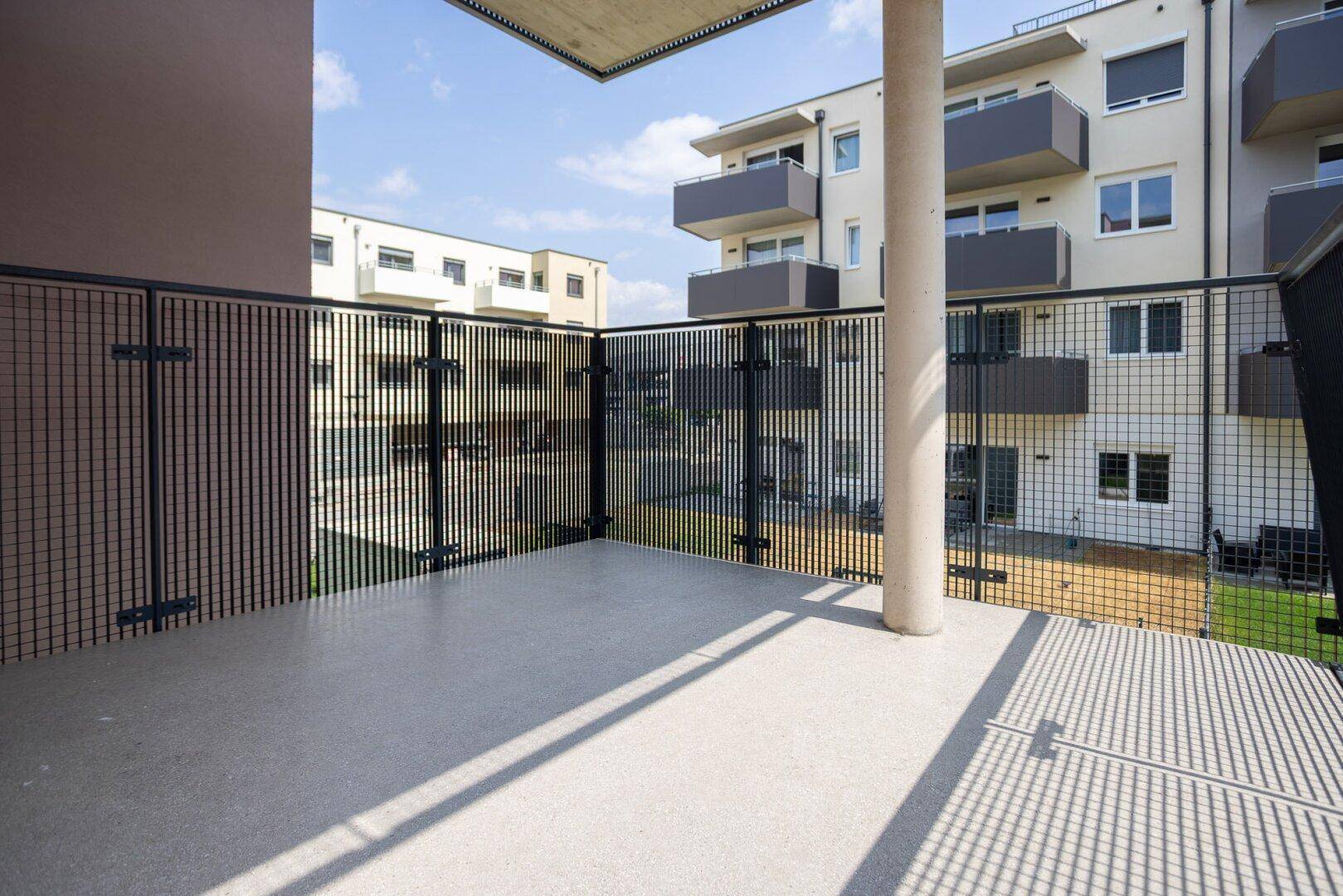 Geräumiger Balkon mit Betonboden und Metallgeländer, umgeben von modernen Wohngebäuden.