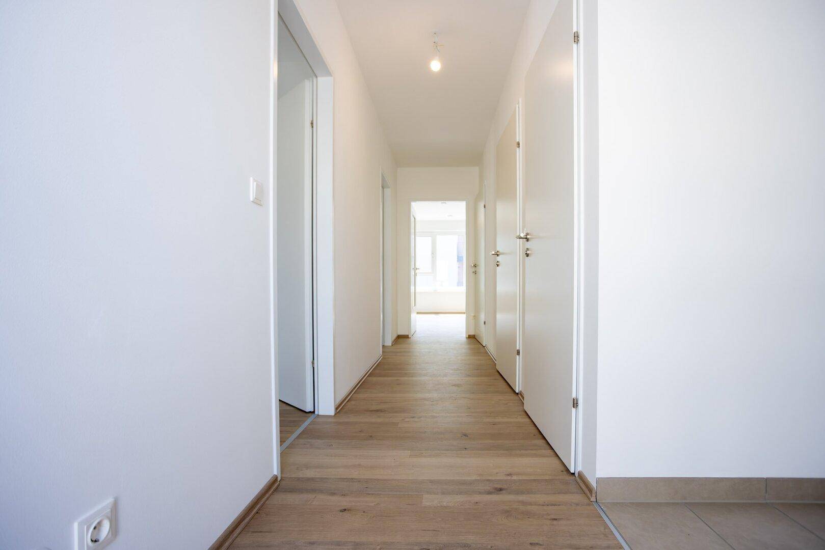 Langer, heller Flur mit Laminatboden und mehreren weißen Türen zu den angrenzenden Räumen.