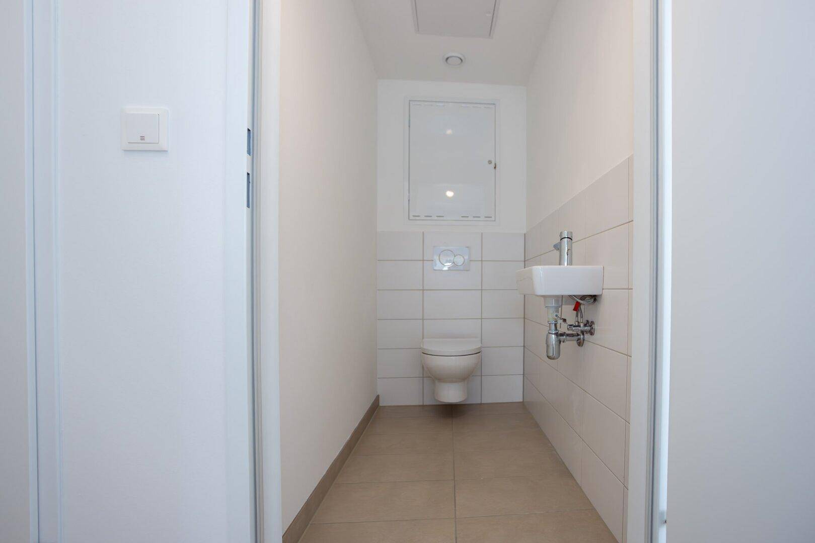 Modernes Gäste-WC mit wandhängender Toilette, kleinem Waschbecken und weißen Fliesen.
