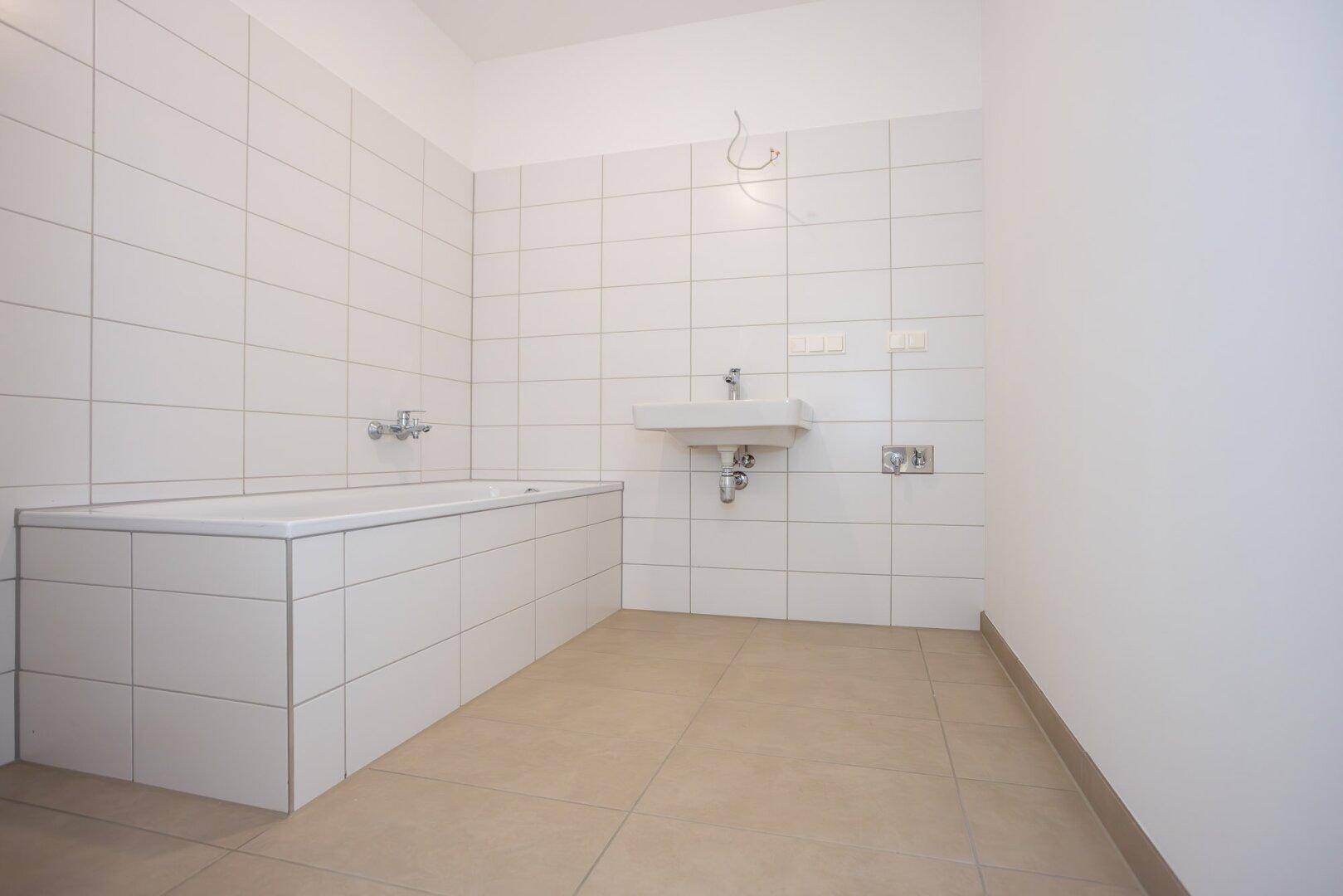Badezimmer mit weißen Fliesen, Badewanne und Waschbecken, bereit für die Endmontage.