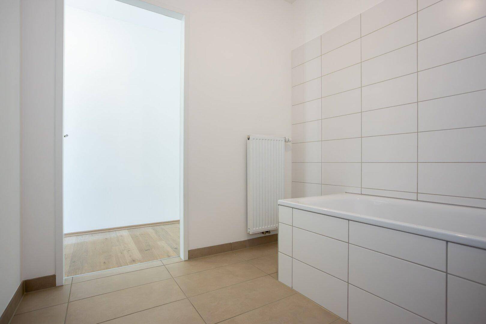 Badezimmer mit weißen Fliesen, Badewanne und Heizkörper, bereit für die Installation der Armaturen.