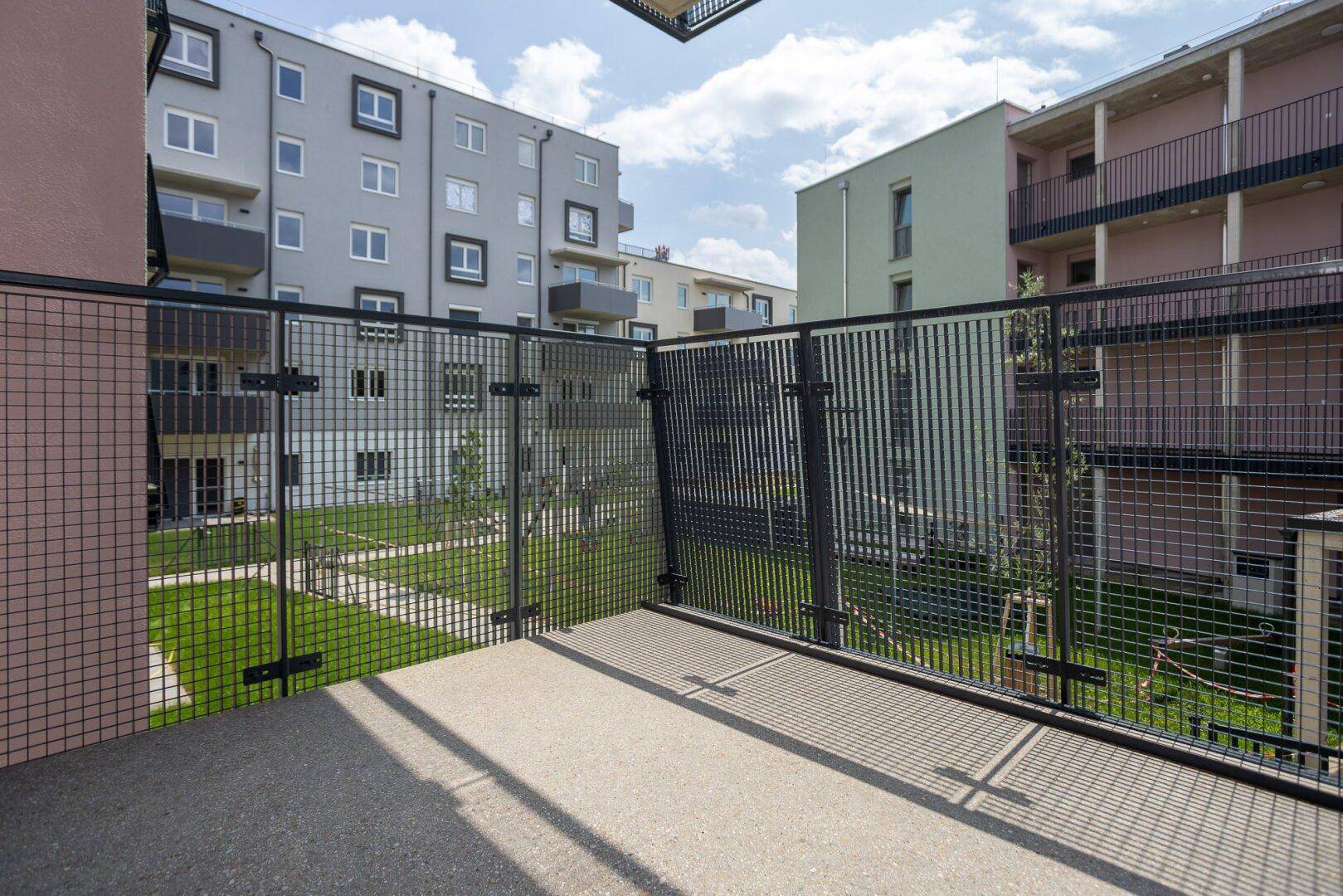 Balkon mit Metallgeländer und Blick auf den begrünten Innenhof der Wohnanlage.