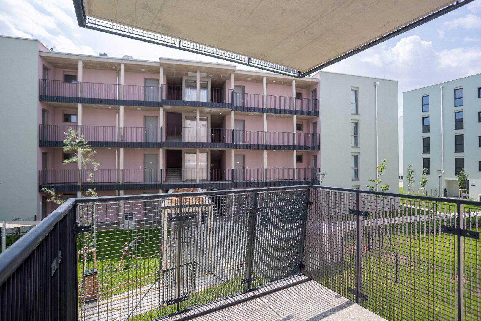 Geräumiger Balkon mit Sonnenschutz und Blick auf den Innenhof der Wohnanlage.