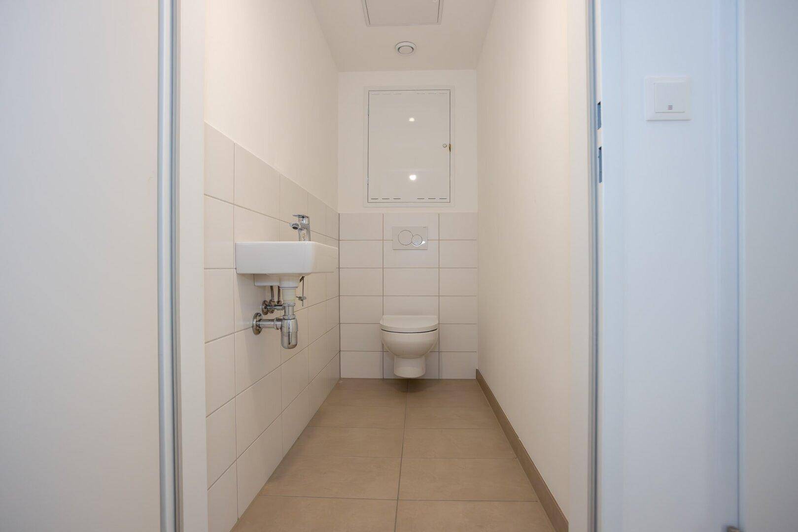 Modernes Gäste-WC mit wandhängender Toilette und kleinem Waschbecken.