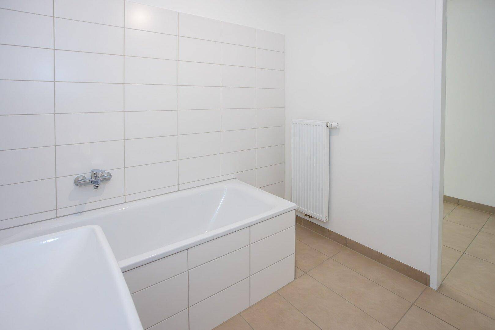 Helles Badezimmer mit Badewanne, Waschbecken und weißen Wandfliesen.