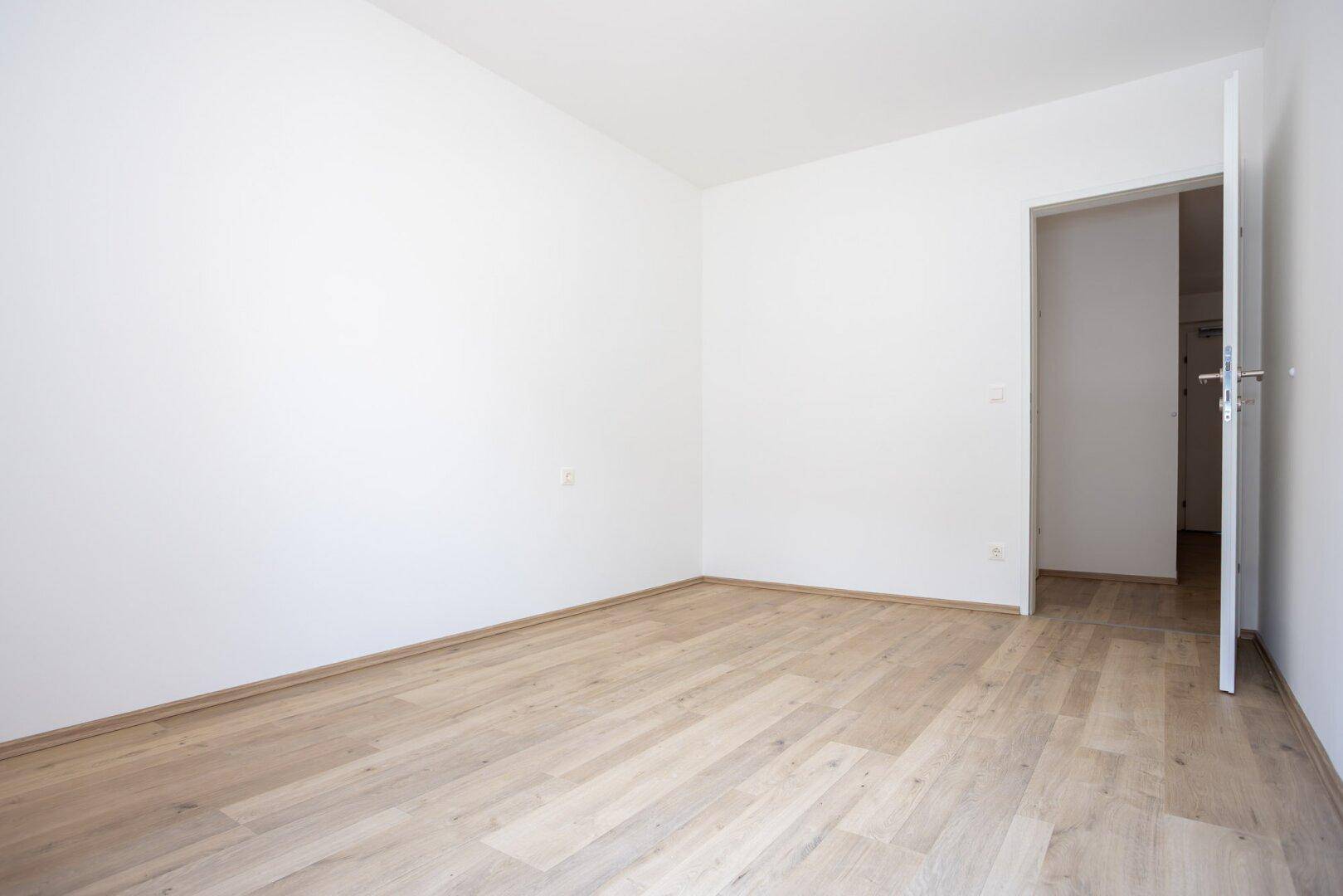 Leeres Zimmer mit Parkettboden und weiß gestrichenen Wänden.