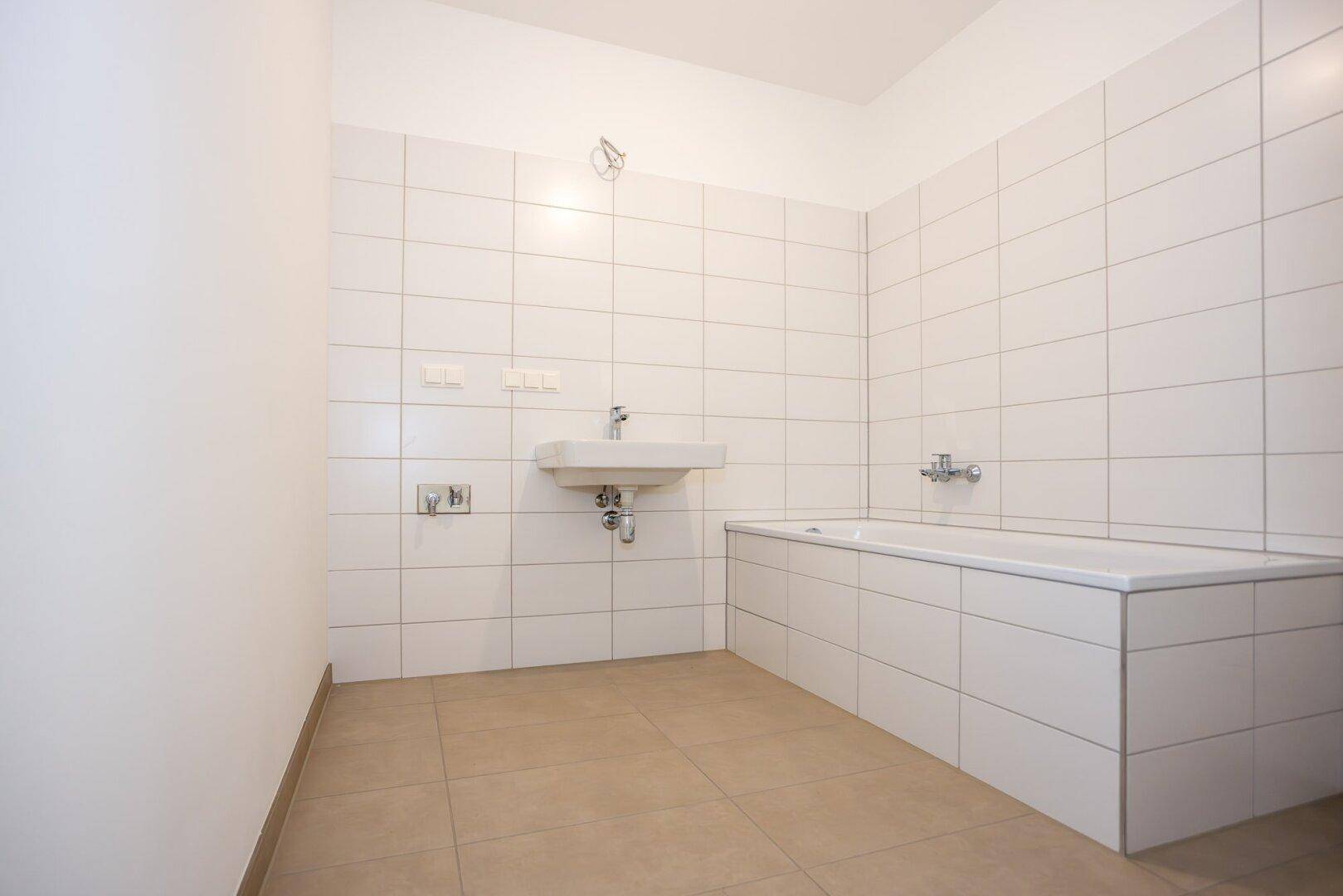 Modernes Badezimmer mit weißen Fliesen, Badewanne und Waschbecken.