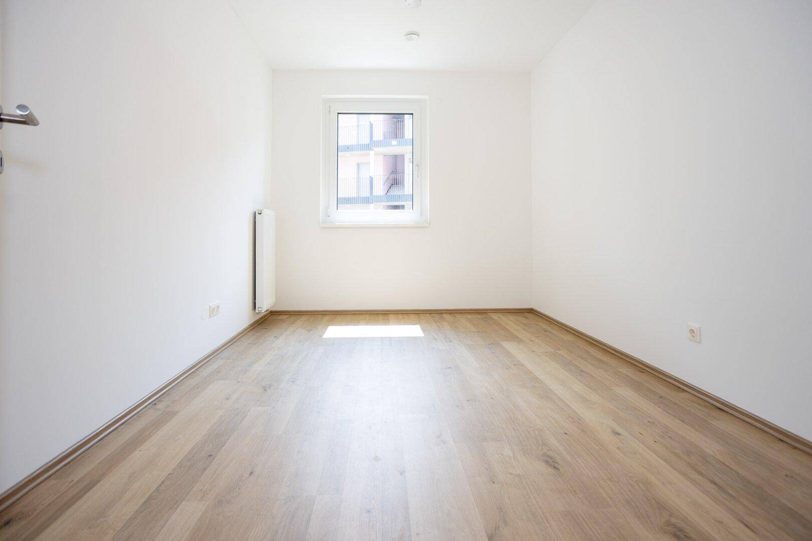 Helles Zimmer mit Parkettboden und Fenster, das viel Tageslicht hereinlässt.