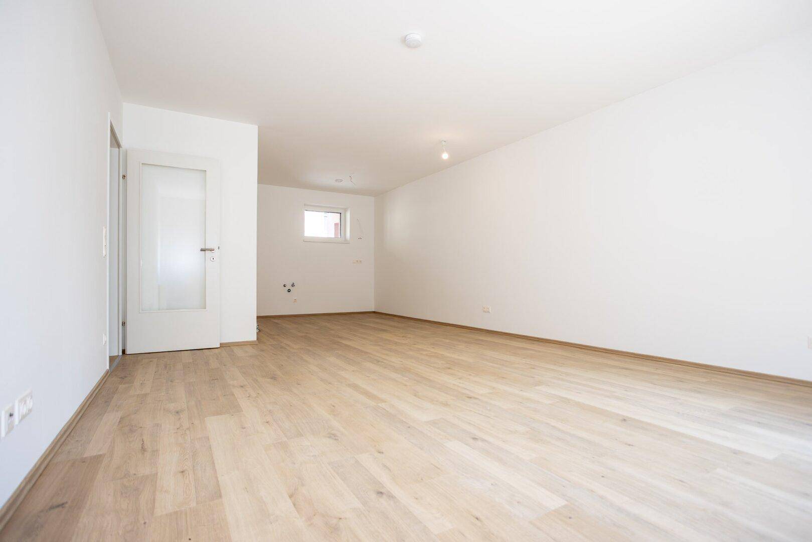 Geräumiges, helles Zimmer mit Parkettboden und Anschlussmöglichkeiten für eine Küche.