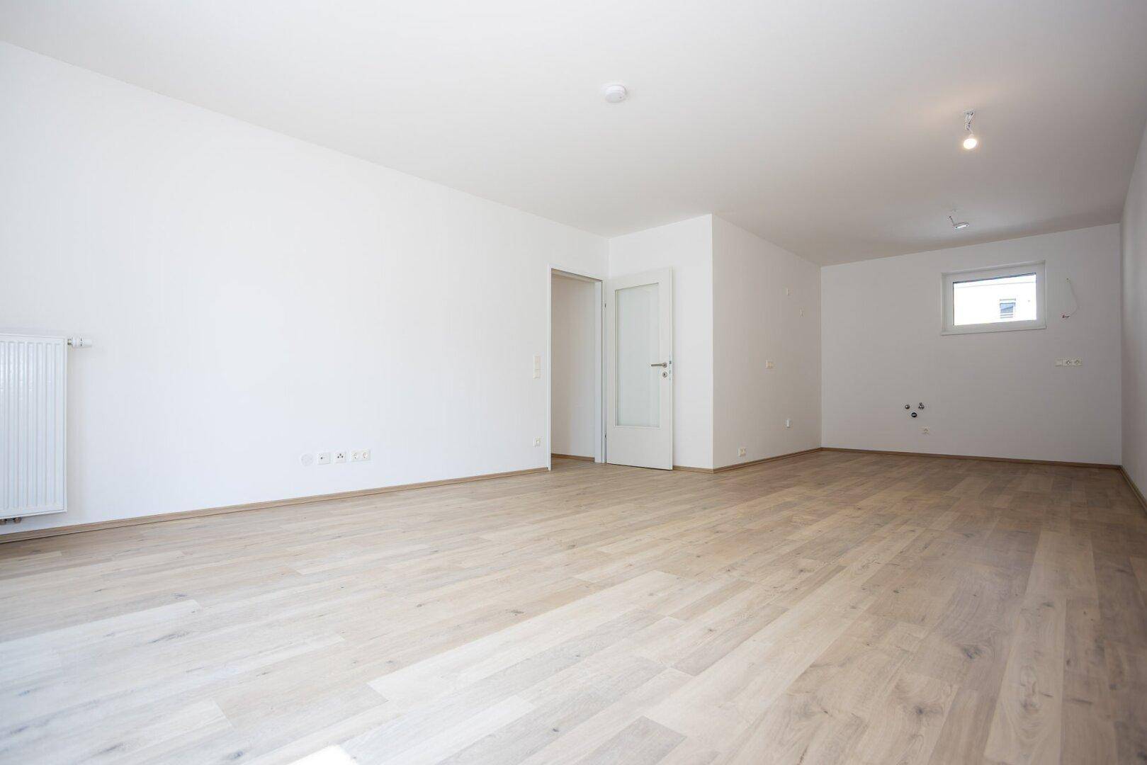 Geräumiges, helles Zimmer mit Parkettboden und Anschlussmöglichkeiten für eine Küche.