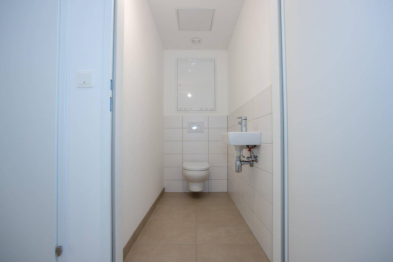 Separates Gäste-WC mit Wand-WC, kleinem Waschbecken und weißen Fliesen, funktional und hell.
