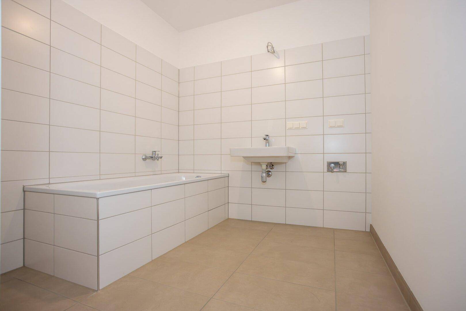 Modernes Badezimmer mit weißen Fliesen, Badewanne und Waschbecken, bereit zur Nutzung.